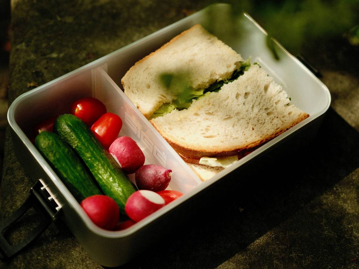 Assorted reusable storage containers for lunch on a kitchen counter with fresh fruits and nuts inside