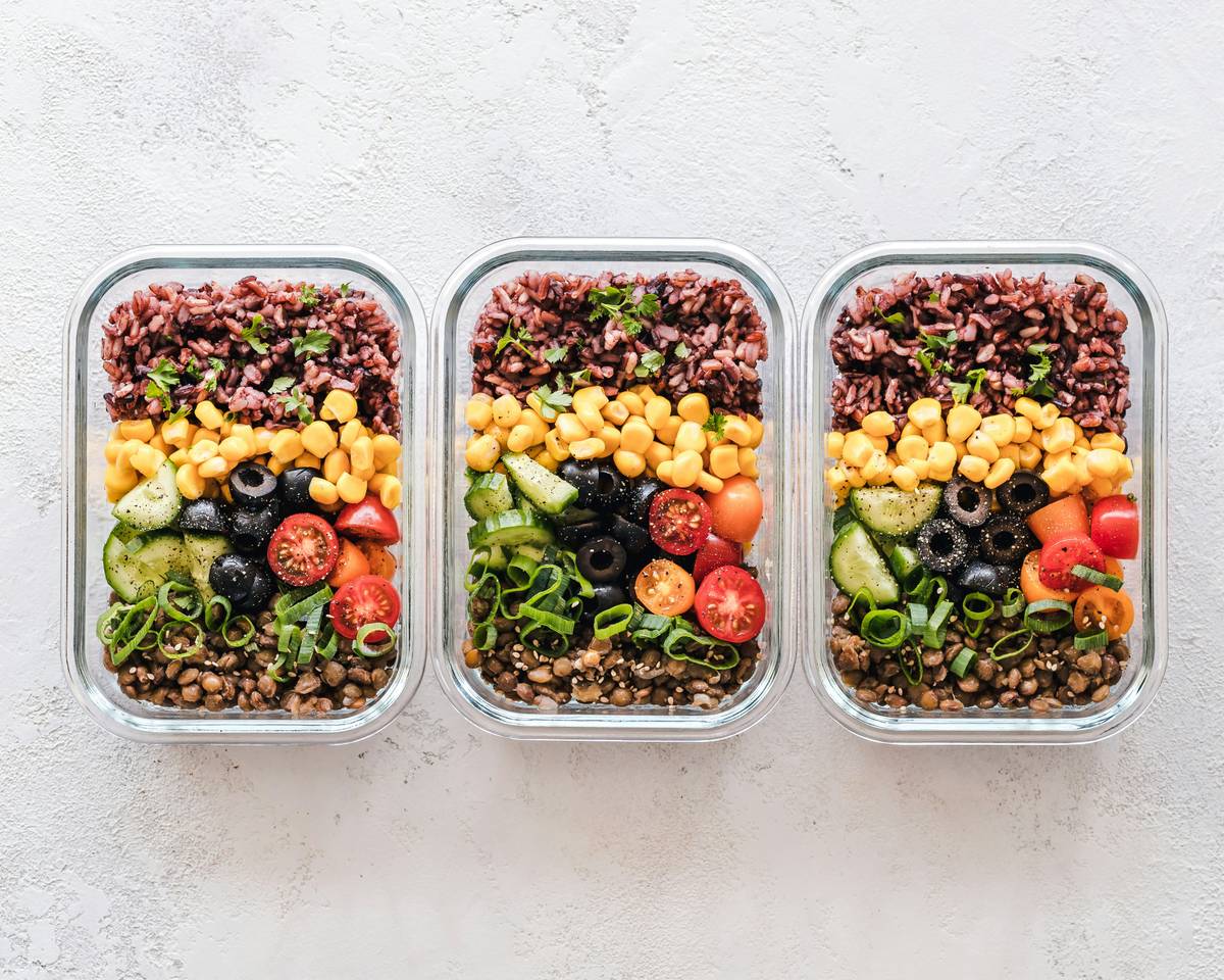 Assorted reusable stainless steel and silicone food containers for lunch arranged on a wooden table with fresh fruit and sandwiches